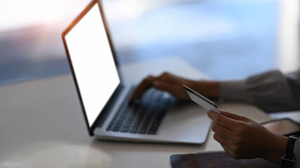 Close up view of woman holding credit card in hand and using laptop for online shopping.