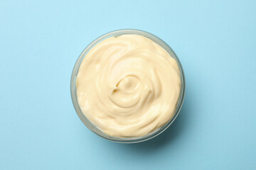 Bowl with mayonnaise sauce on blue background
