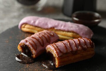 Tasty eclairs with delicious topping on black tray, close up