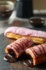 Tasty eclairs with delicious topping on black tray, close up