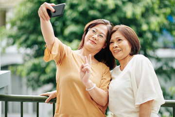 Fototapeta premium Senior smiling Asian women taking selfie on smartphone when standing outdoors
