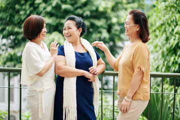 Group of senior Vietnamese female friends standing on balcony, discussing news and joking around