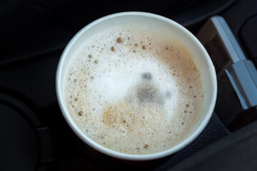 Cappuccino in a paper cup in the car. Morning delicious coffee to take away. Top view of the foam and a beautiful pattern. Paper disposable cup. Creamy foam, fragrant coffee close-up. Stale coffee