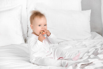 Cute little baby with teething toy sitting on bed