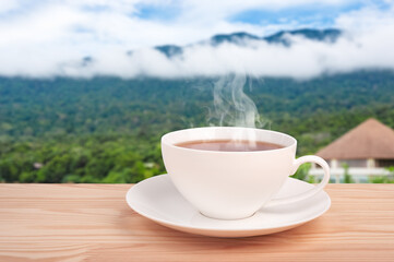 Tea cup with organic tea leaf on the wooden table and tea plantations. Morning cup of tea with mountain jungle background