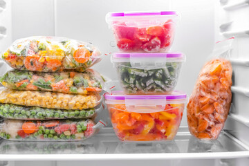 Containers and plastic bags with frozen vegetables in refrigerator