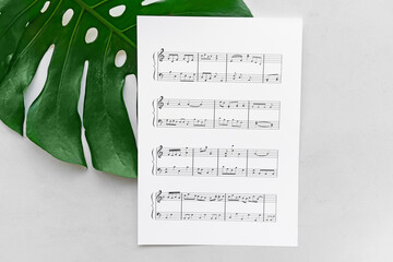 Paper sheet with music notes and green leaf on light background
