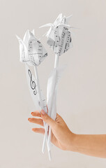 Female hand with paper flowers made of music sheets on light background