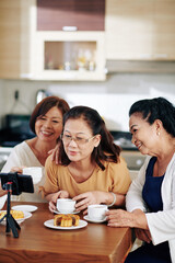 Smiling elderly Asian women drinking tea with pastries and recording video for their channel