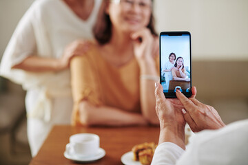 Close-up image of senior woman photographing her hugging female friends on smartphone