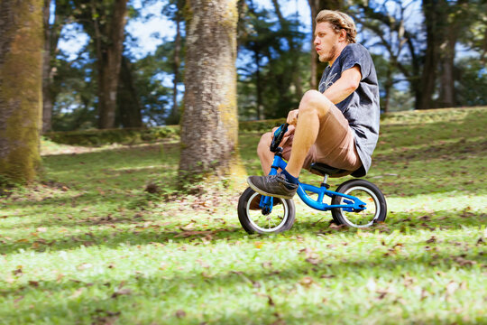 Funny downhill on small kids balance bike. Young crazy man riding down from high hill.