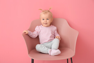 Portrait of cute little baby girl sitting in armchair on color background