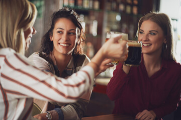 Three happy girlfriends are having fun time in pub. They are talking and drinking beer. Friendship concept.
