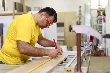 Carpenter taking measurement of a wooden plank with pencil and ruler
