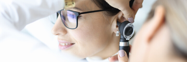 Otolaryngologist doctor examining patients ear with otoscope in clinic. Diagnosis of otitis media concept