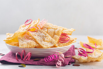 Angel wings or sfrappole or chiachiere. Traditional sweet crisp pastry deep-fried and sprinkled with powdered sugar. Carnival food tradition. Decorated with paper serpentine.