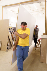 Two men carry furniture materials in their workshop