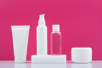 Obraz na płótnie Canvas Set of beauty products in a row on white glossy table against bright pink background. Concept of skin care and beauty 