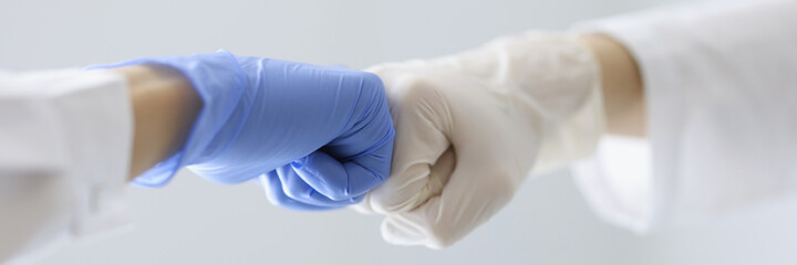 Doctors in rubber gloves touching their fists in clinic close-up. Health care workers cooperation...