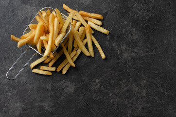 French fries in metal wire basket over white kitchen table.