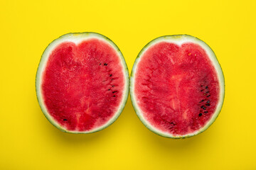 Fresh red watermelon cut in half on a bright yellow background.