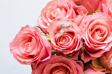 Two wedding rings placed on the bouquet of pink roses for Valentine's day on white background.