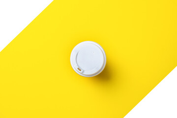 White lid on a cardboard glass from above on a yellow-white background. Flat lay, top view.