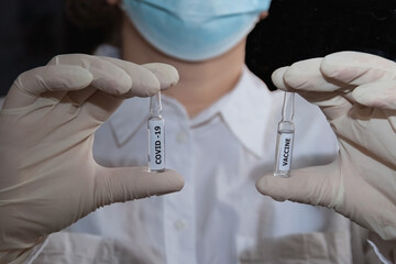 A woman in a white medical coat and mask holds vials of the Covid-19 vaccine in her hands
