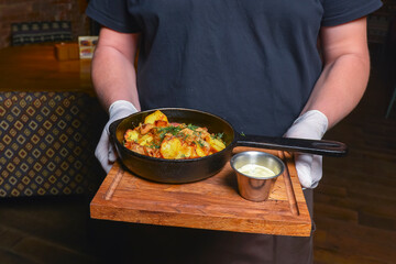 Fried potatoes in an iron pan served in a restaurant or diner. Waiter service, eating out concept.