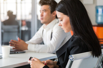 Young woman in business suit at the table uses smartphone