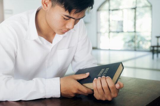 Man praying, hands clasped together on her Bible.