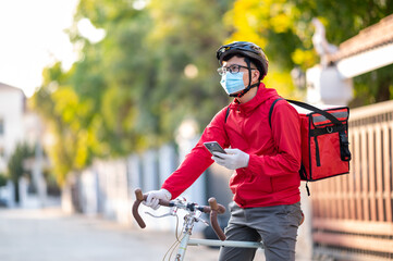 Delivery man wearing face protective mask to avoid corona virus Look at the phone to find the customer address through the application.