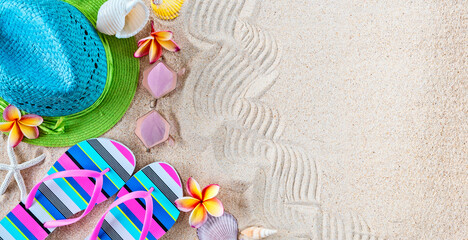 Blue and green straw Hat and colorful Flip Flops in the sand with shells and frangipani flowers. Summertime on beach concept.