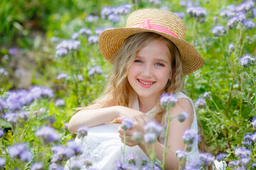 little girl in a straw hat in a purple field in summer