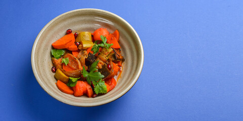 Baked vegetable salad in a cermaic bowl over blue background. Delicious healthy autumn or winter salad.
