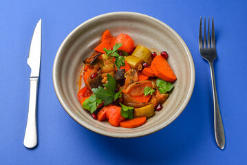 Baked vegetable salad in a cermaic bowl over blue background. Delicious healthy autumn or winter salad.