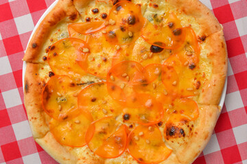 Pizza with persimmon. Italian cuisine concept flat lay, top view. Persimmon dishes menu over red plaid tablecloth.