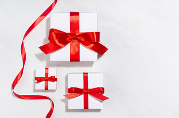 Minimalist elegant three New Year white gift boxes with red bow on white wood board as border, top view.