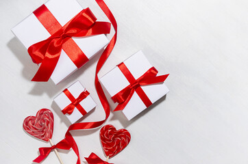 Bright birthday background with love - white gift boxes with red bow, curl ribbon, lollipops hearts on white wood board, border, closeup.