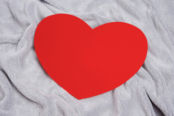 Red heart on a gray bedspread or a blanket, top view