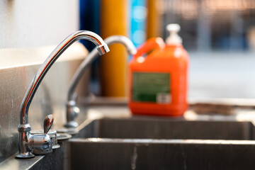 Hand washing sink station in chemical factory. Close-up and selective focus at the faucet outlet with blurred of liquid cleaner pumping box as background.