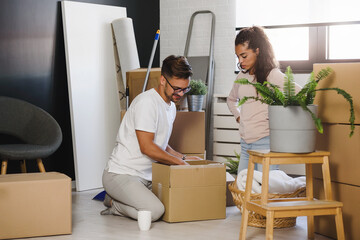 Happy multiethnic couple just moved into new empty apartment unpacking, cleaning, enjoying new...