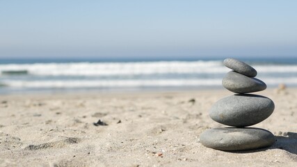 Rock balancing on ocean beach, stones stacking by sea water waves. Pyramid of pebbles on sandy shore. Stable pile or heap in soft focus with bokeh, close up. Zen balance, minimalism, harmony and peace