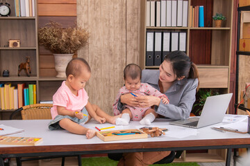 Beautiful Asian single mother happy playing with adorable kids while working at home, children play peekaboo with fun on mother working desk, multi-task young freelancer woman with daughters concept