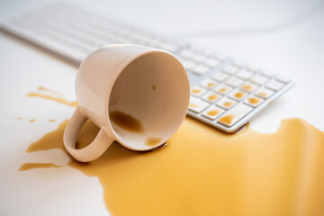 Spilled black coffee on a computer keyboard at a white table