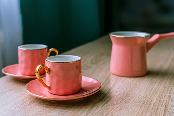 Pink ceramic coffee set - turk and two cups on wooden table. Tableware in the English style