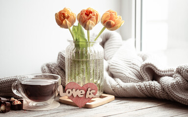 Cozy composition for Valentine's Day with a drink in a cup and flowers in a vase.