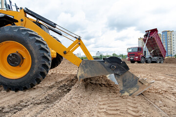 Fototapeta premium Wheel loader Excavator Machine wih Multi-Purpose bucket levelling Construction Site during Earthmoving Works on Truck unloading sand background
