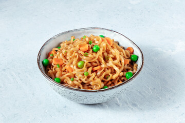 Instant noodles in a bowl, with green peas and carrots
