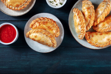 Empanadas with sauces, shot from the top with copy space on a dark blue rustic wooden background